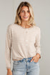 A woman wearing a beige and white horizontally striped button-up cardigan sweater with light blue jeans, standing against a light gray brick wall.