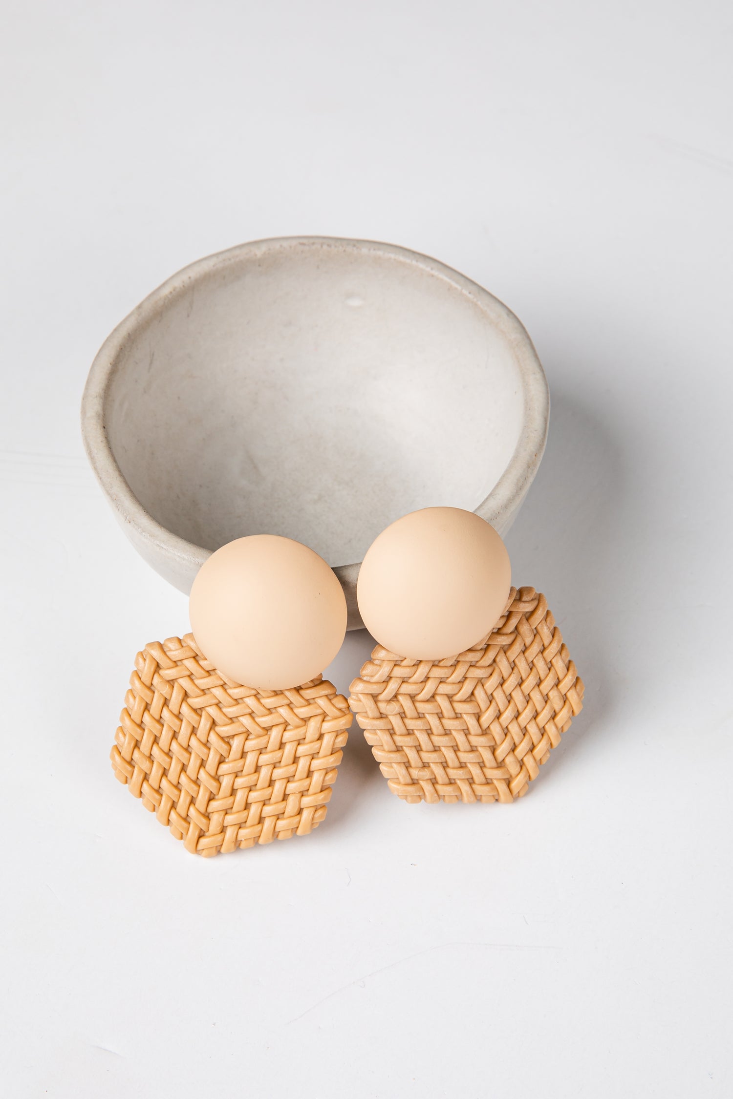Pair of earrings with woven design and round beige stones on a light gray background