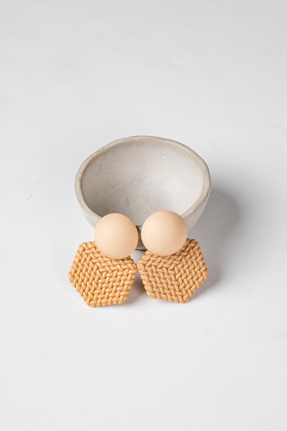 Pair of earrings with woven design and wooden beads on a light gray background