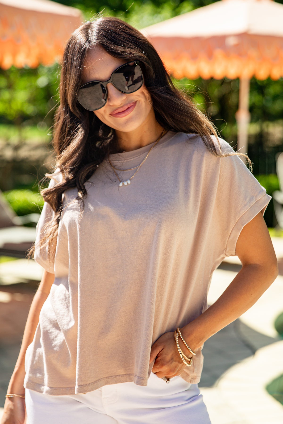 Woman wearing sunglasses and a beige top with white pants outdoors.