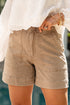Person wearing beige shorts and a white blouse with a blurred background
