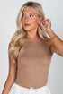 Woman wearing a brown tank top and white pants against a plain background