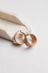 A pair of chunky, matte-finish hoop earrings in a warm beige/tan color, resting on a white stone tray against a clean white background.