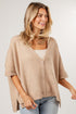 A woman wearing a beige knit cardigan with short sleeves and front buttons, paired with a white top and light blue jeans, photographed against a light gray studio background.