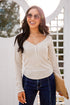 Woman wearing a beige sweater and blue jeans, standing outdoors with a blurred background