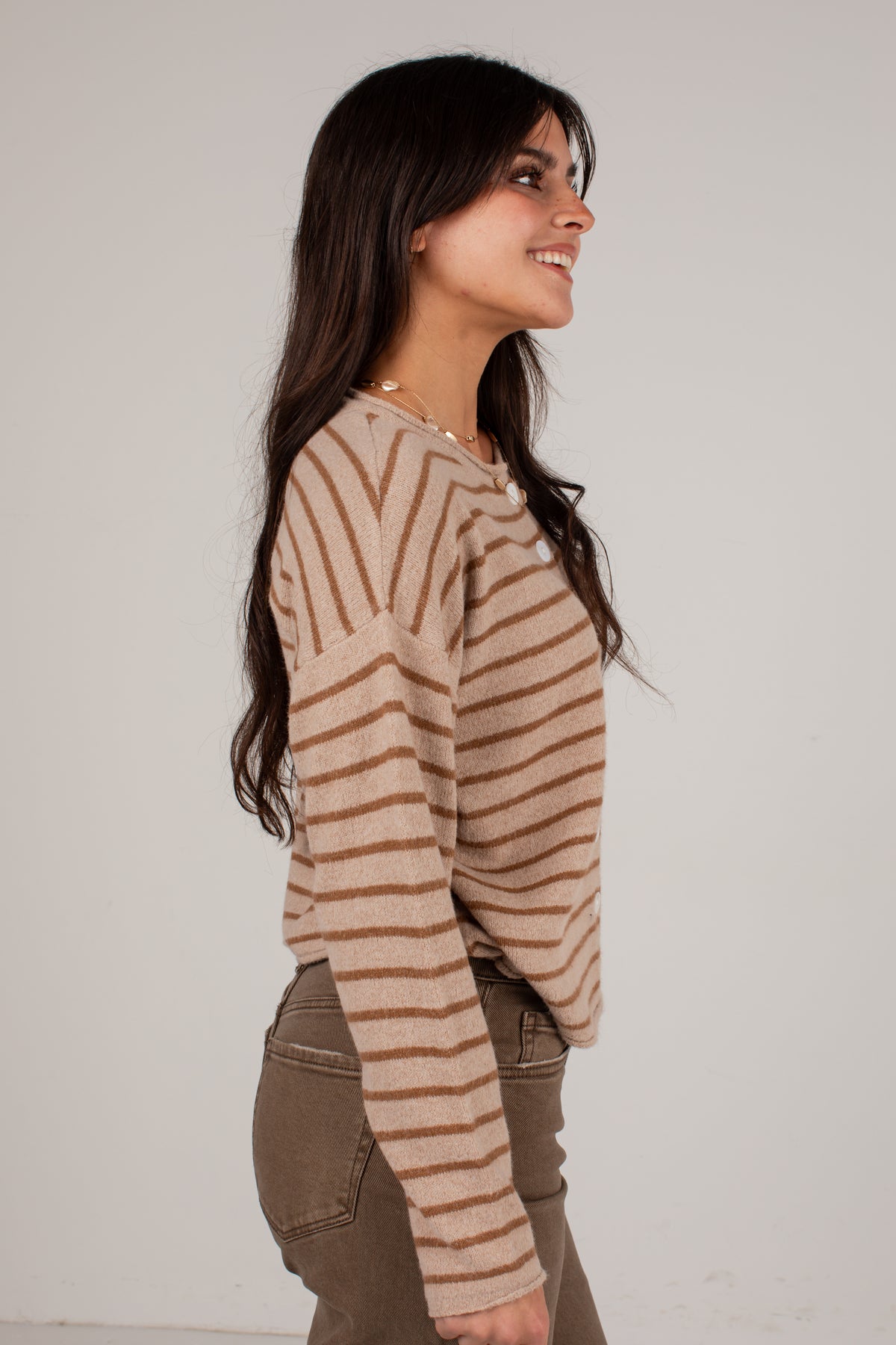 A woman wearing a beige and brown striped knit sweater, shown in profile against a plain light gray background.