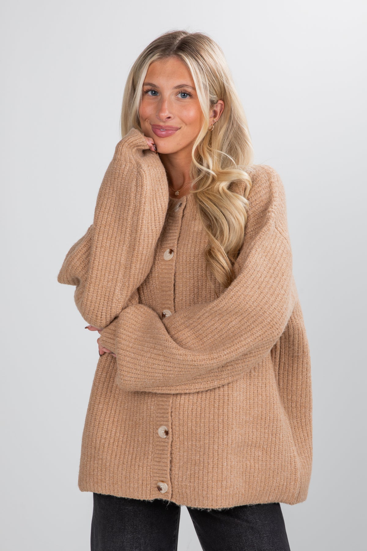 Woman wearing a beige cardigan against a plain background