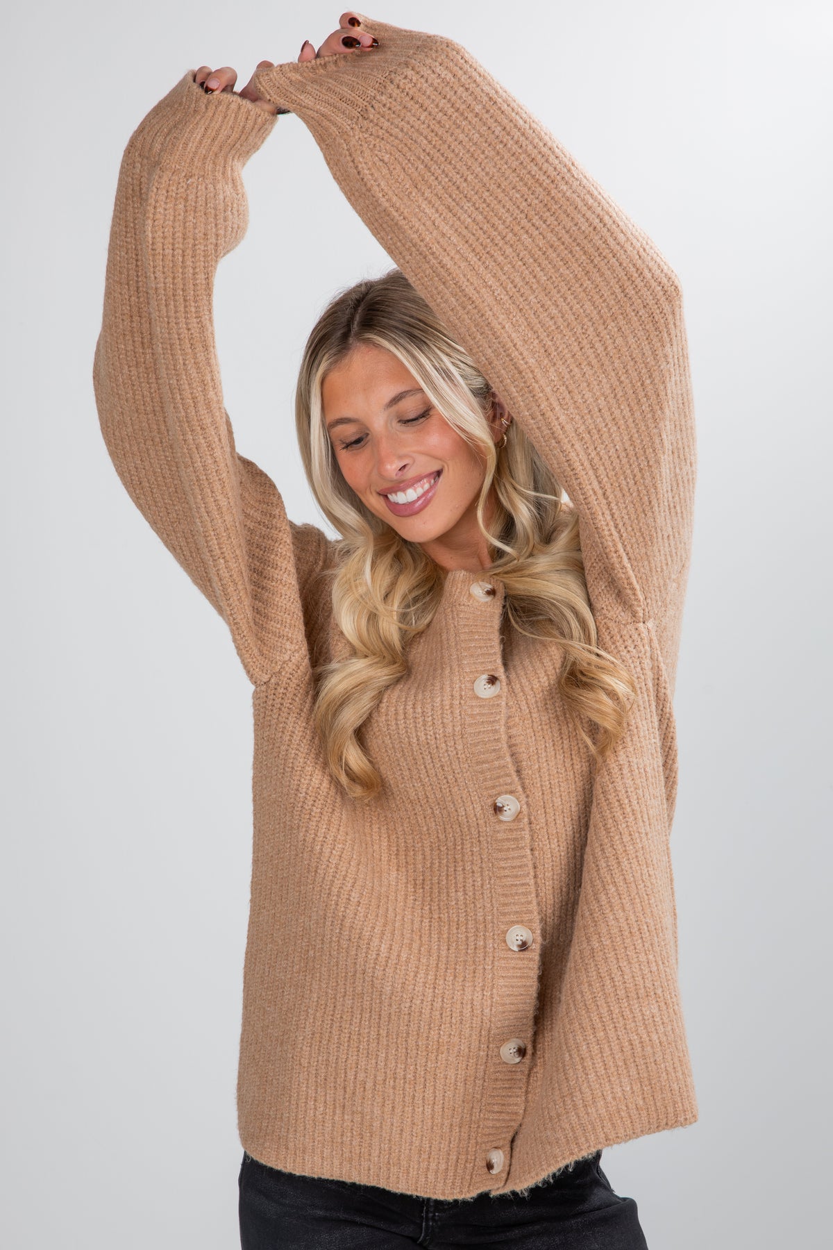 Woman wearing a beige cardigan with button details on a plain background