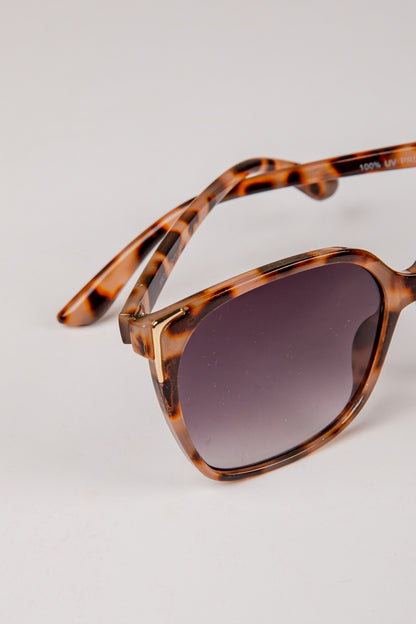 Sunglasses with tortoiseshell frame and dark lenses on a light gray background