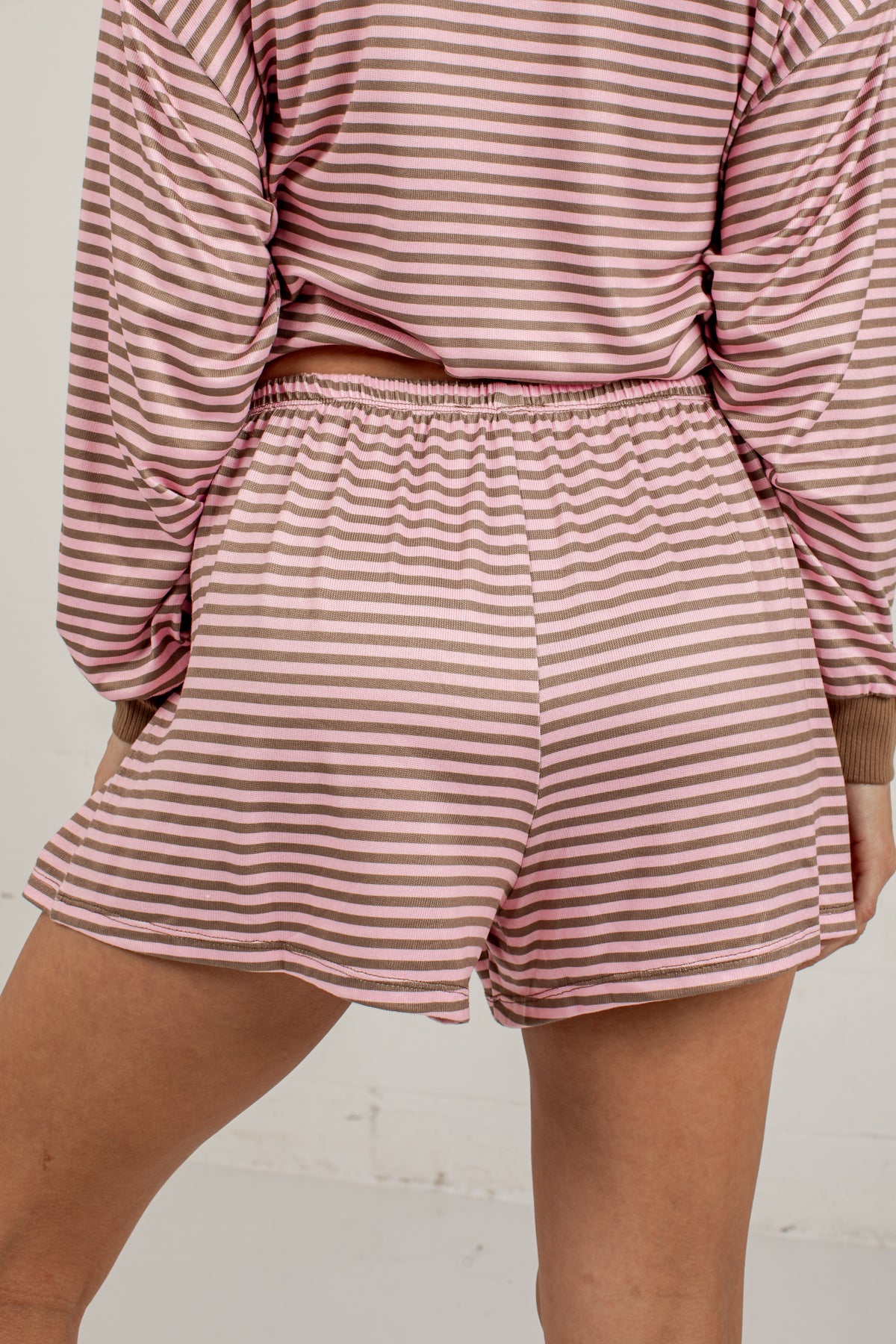 A close-up of a person wearing a matching two-piece loungewear set with long-sleeve cropped tops and high-waisted shorts, both in a dusty rose pink and white horizontal stripe pattern.