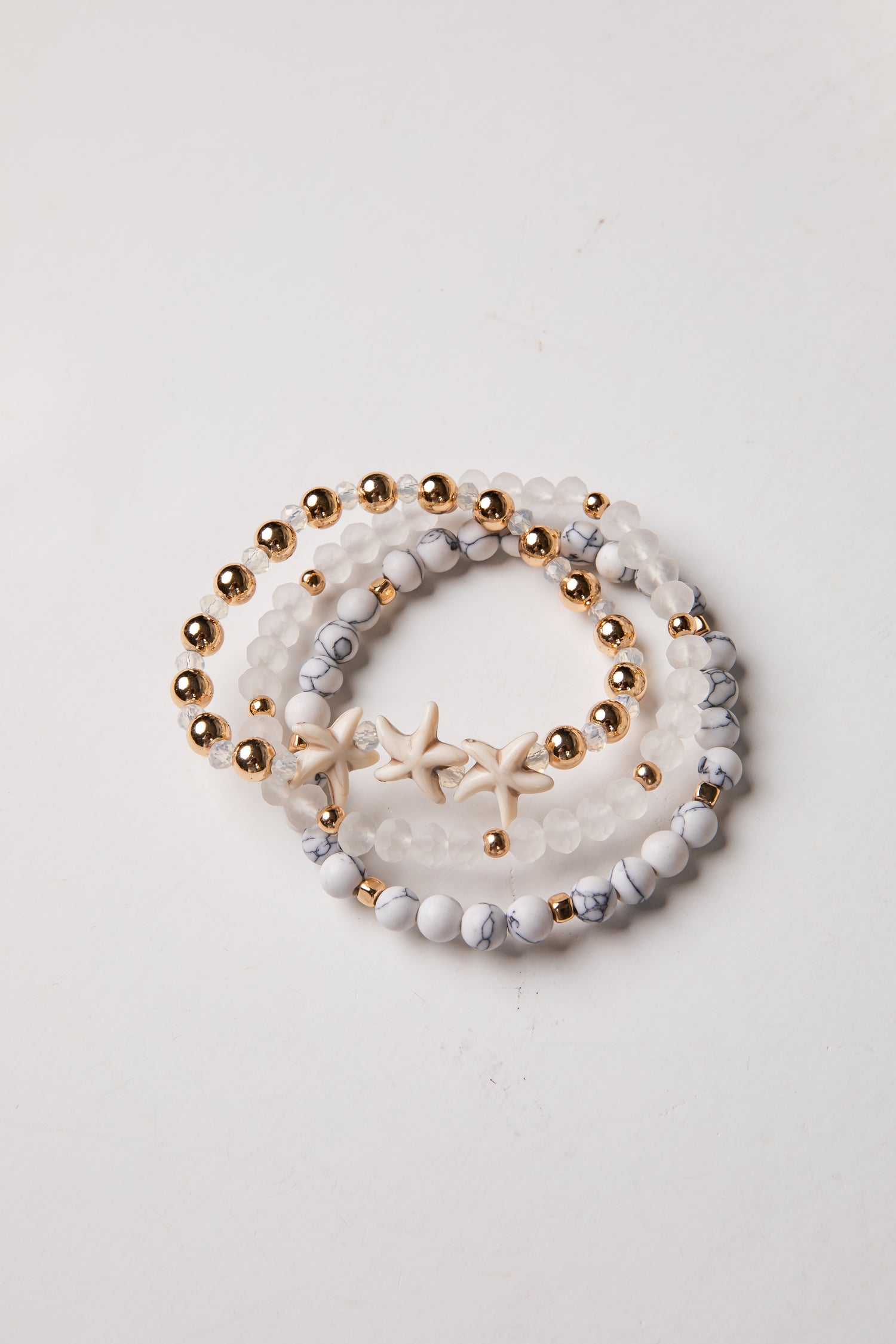 Set of three beaded bracelets with gold beads and starfish charm on a light background