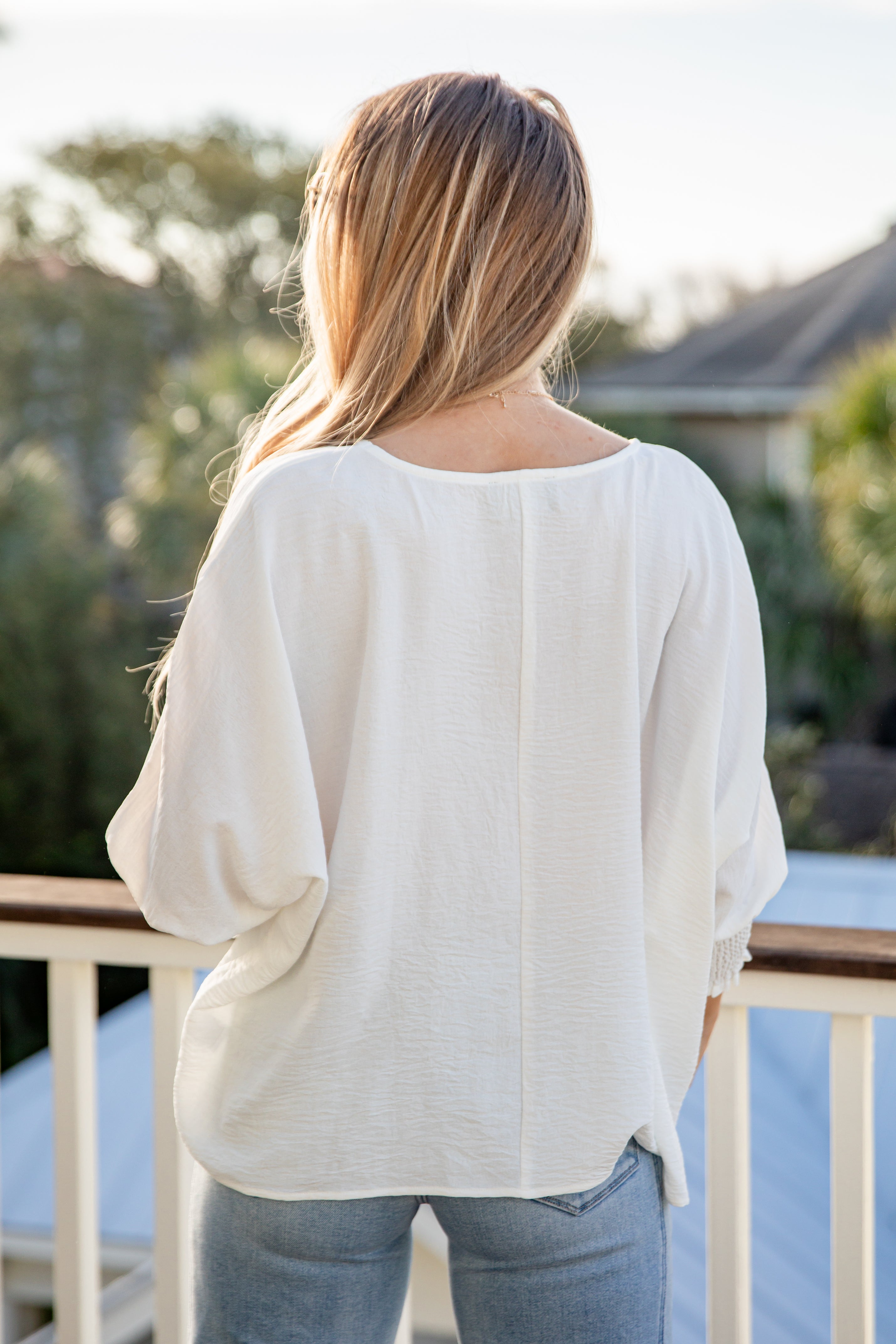 Person wearing a white blouse and jeans standing on a deck with blurred background