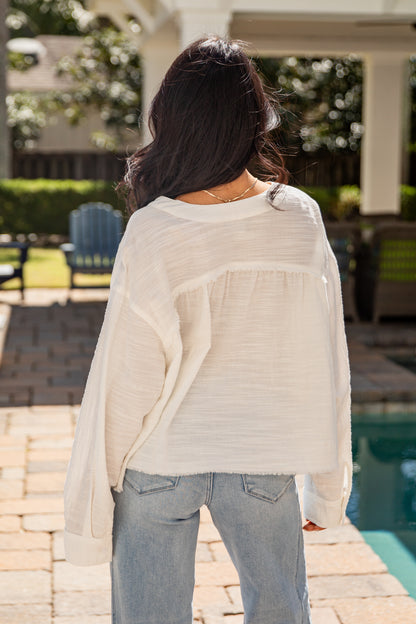 Person wearing a light-colored blouse and jeans standing by a poolside.