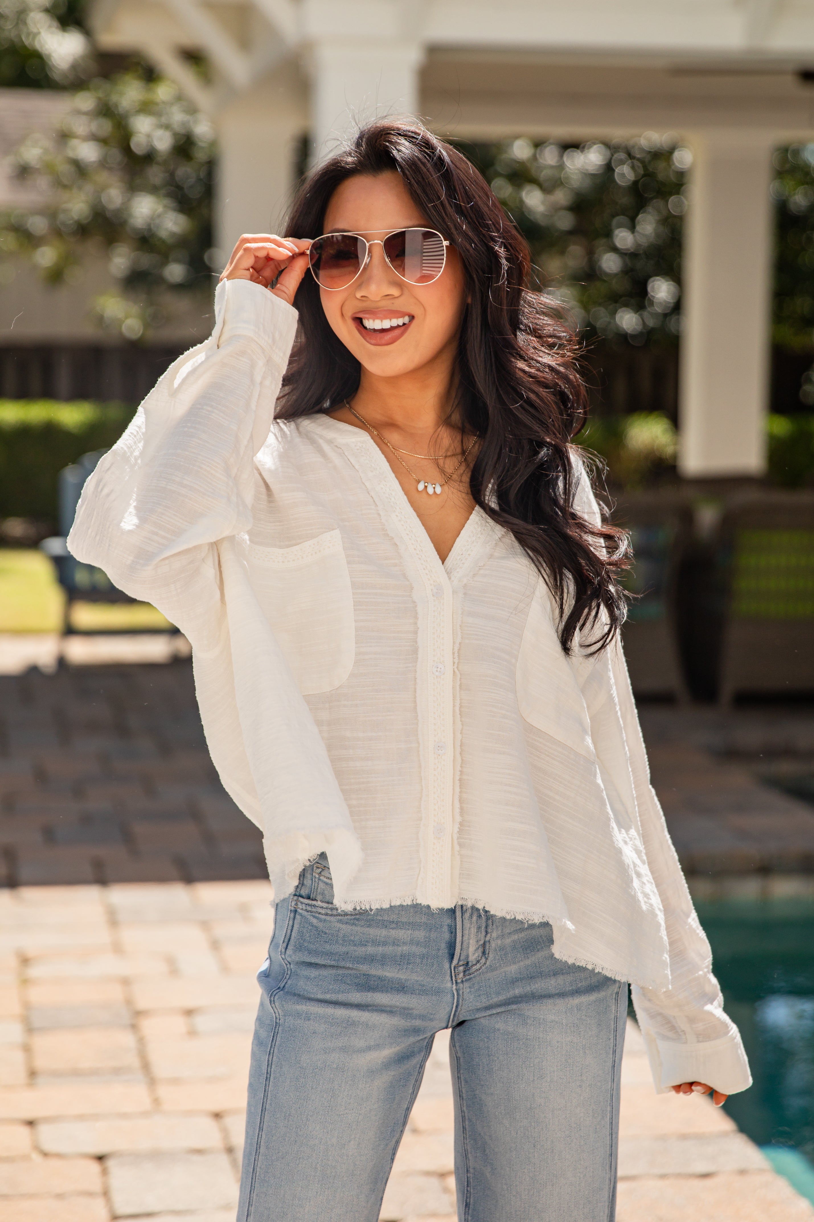 Woman wearing a white shirt and sunglasses outdoors near a pool