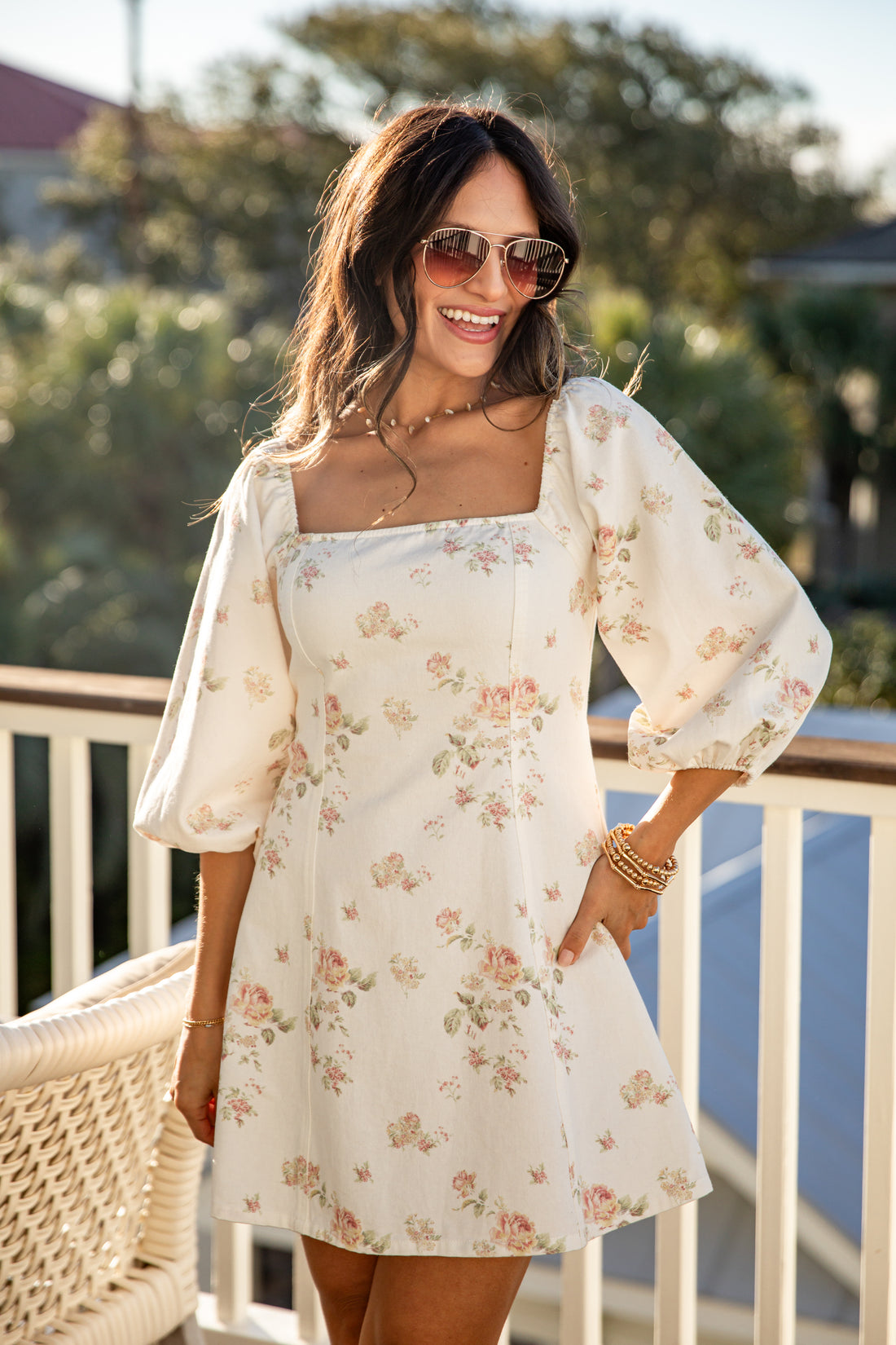 Woman wearing a floral dress on a balcony with greenery in the background