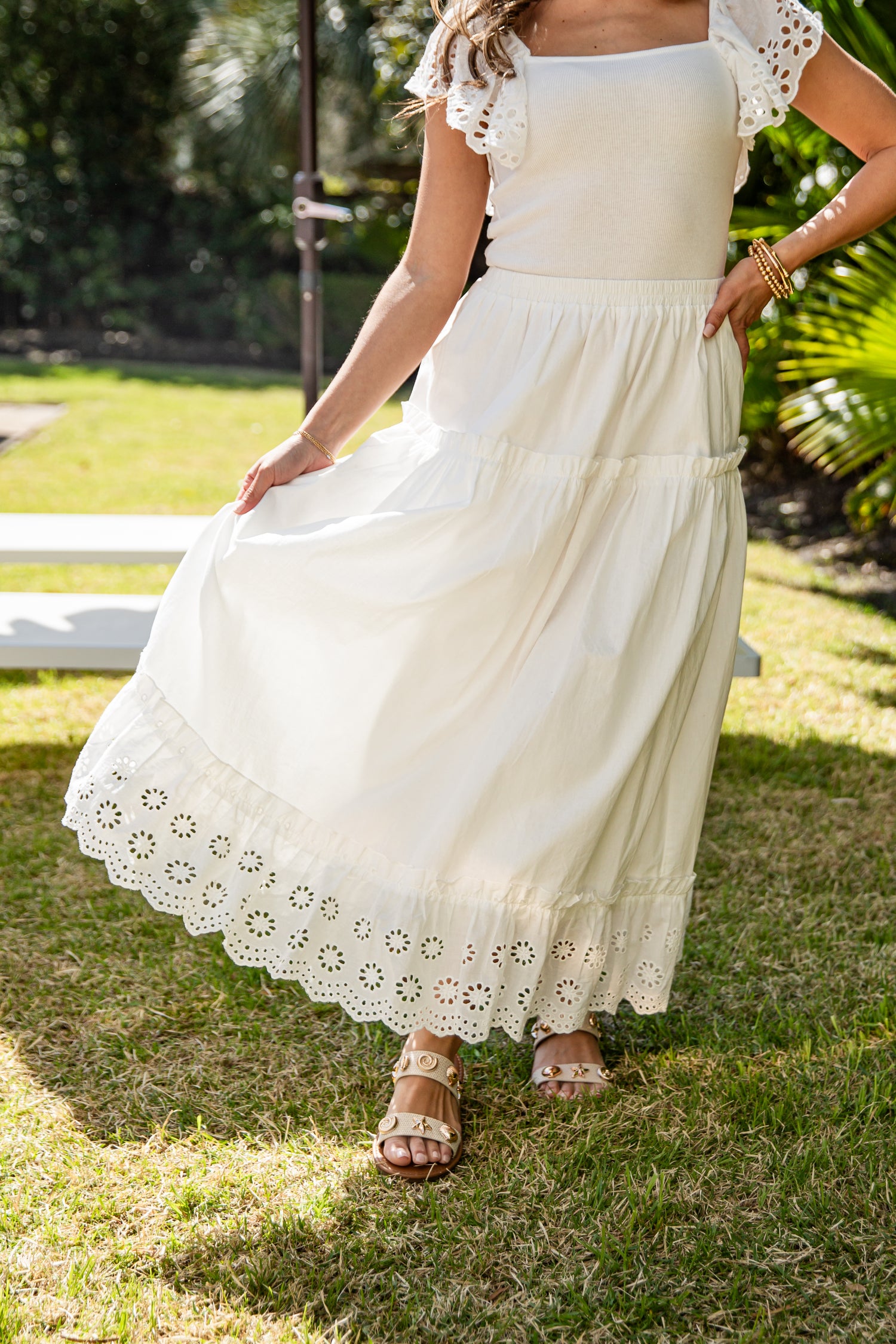 Woman wearing a white dress with lace details standing on grass.
