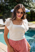 Woman in white top and red patterned shorts smiling poolside.