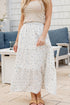 Woman wearing a long floral skirt and beige top in an outdoor setting.