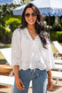 Woman wearing a white blouse and blue jeans standing in a garden setting with umbrellas and lounge chairs.