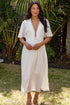 Woman in a white dress standing outdoors with greenery in the background