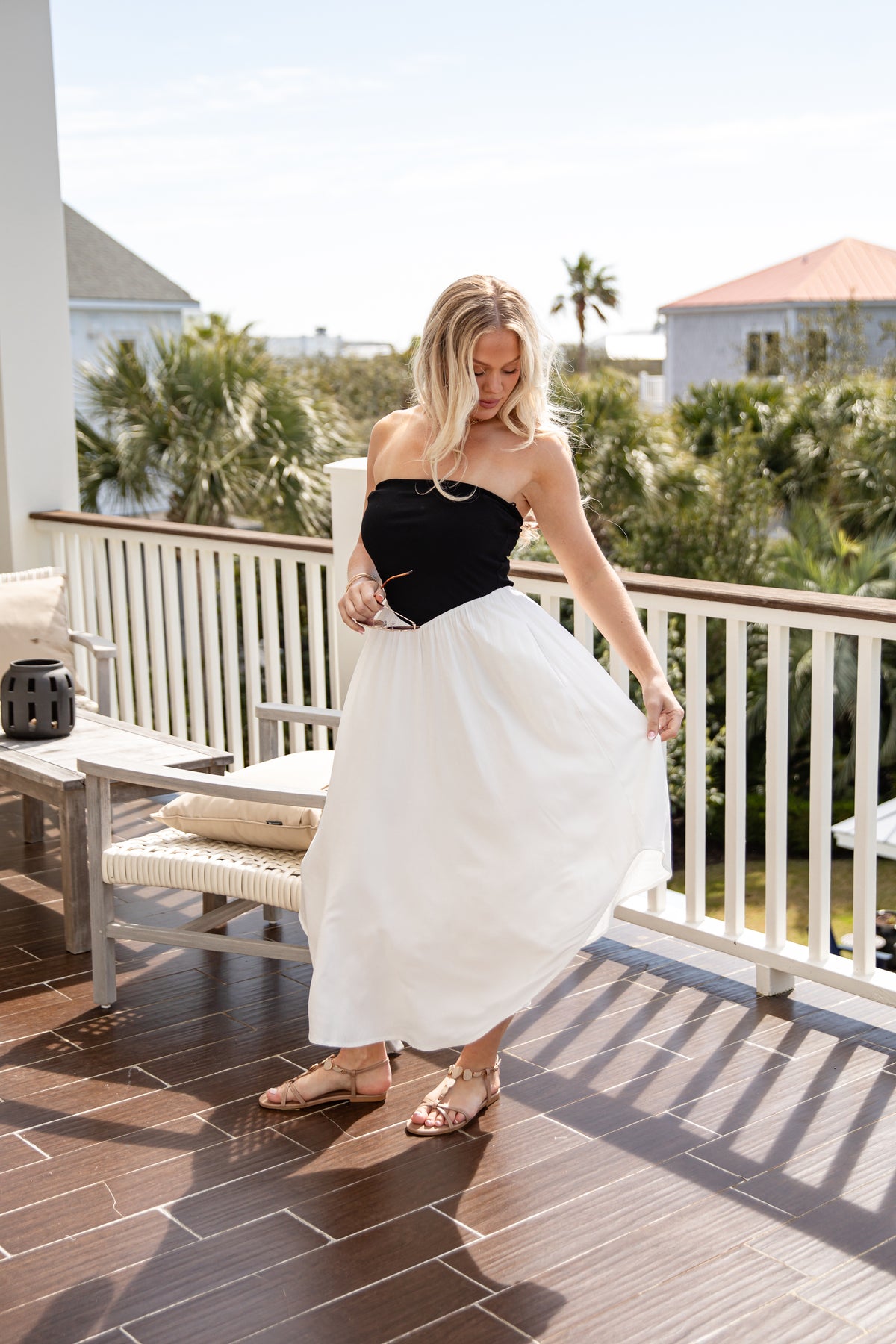 Woman in a black top and white skirt standing on a balcony with greenery in the background