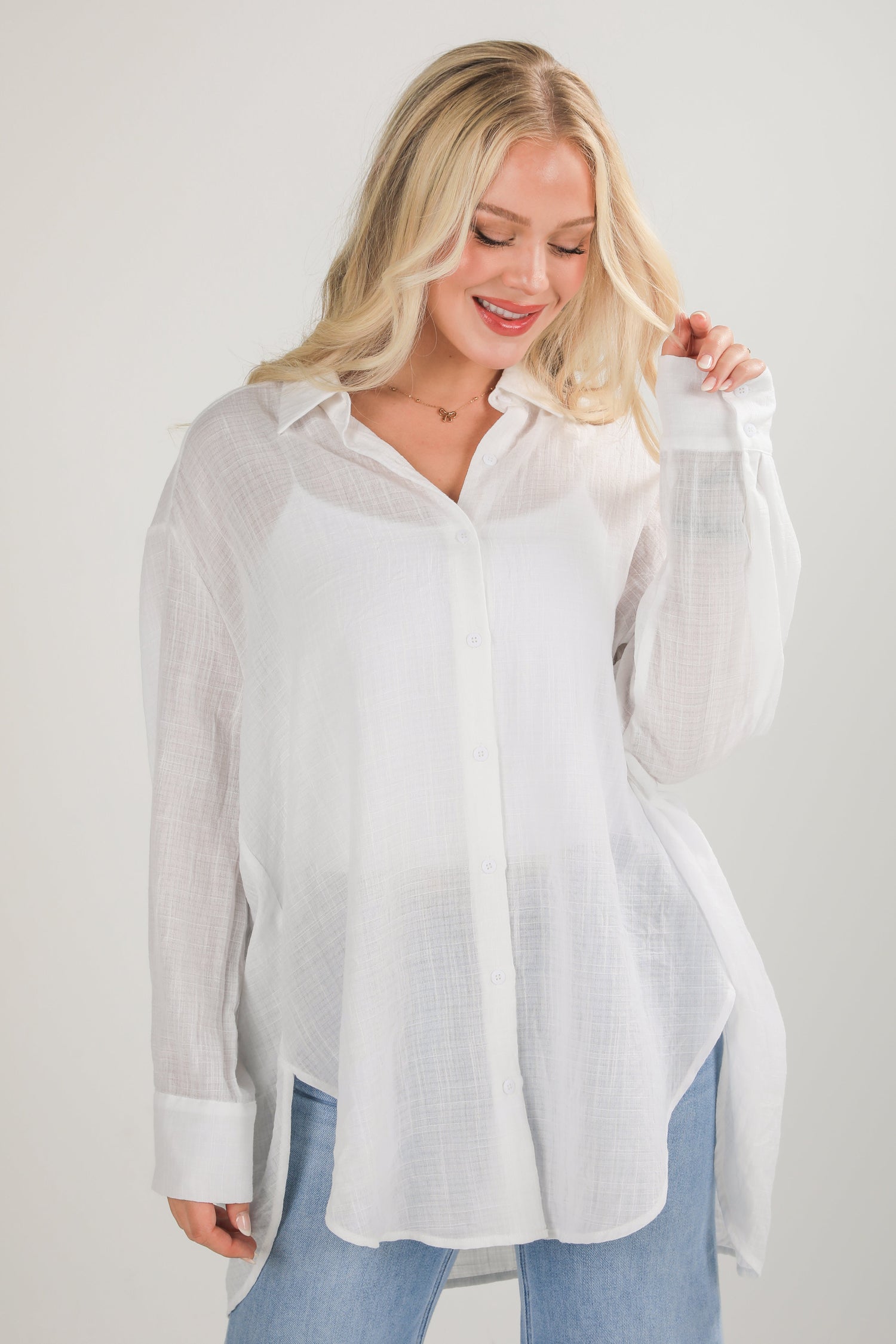 Woman wearing a white button-up shirt with sheer sleeves against a plain background