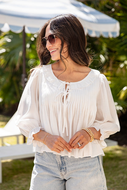 Woman wearing a white blouse and sunglasses outdoors with greenery in the background
