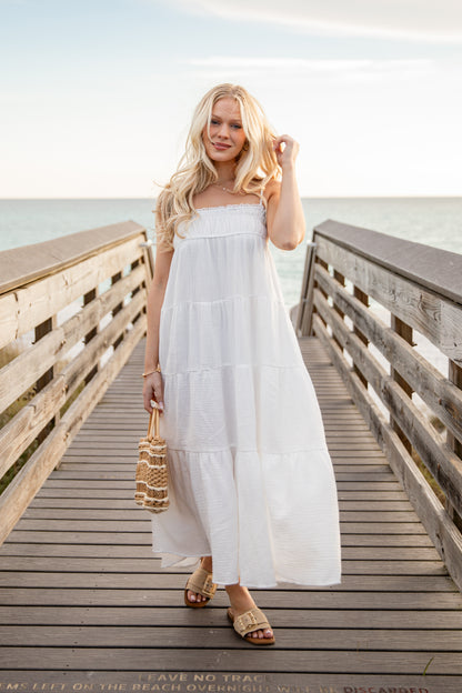 Woman in a white dress standing on a wooden pier by the sea.