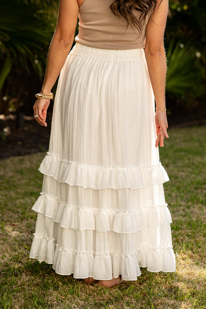 Woman wearing a beige top and white ruffled skirt outdoors.