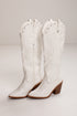A pair of white leather cowboy boots with decorative stitching, silver studs, and brown stacked block heels, shown against a plain light gray studio background.