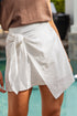 Person wearing a brown top and white wrap skirt by a pool