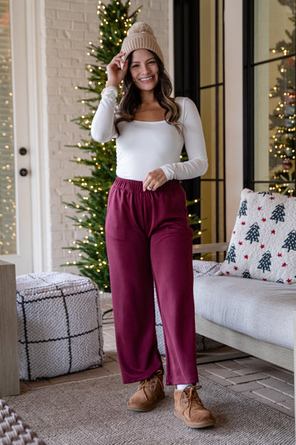 Girl wearing burgundy pants standing in front of a Christmas tree
