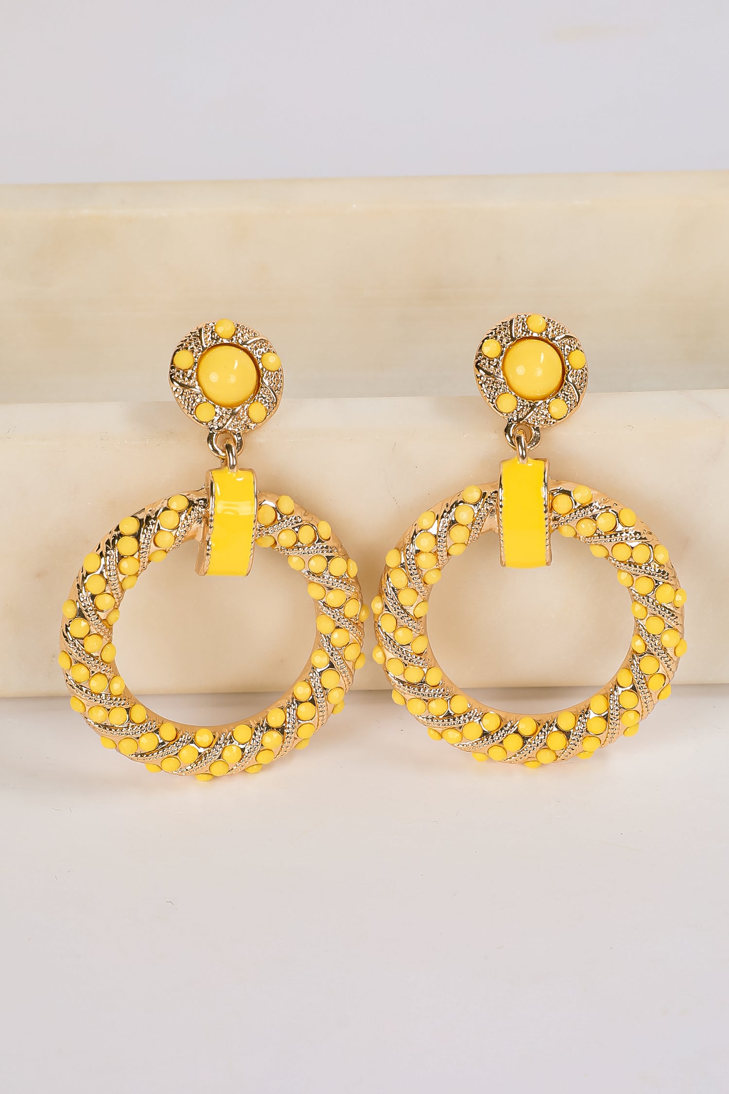 Pair of yellow hoop earrings with intricate designs on a light background