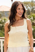 Woman wearing a light yellow top and white skirt on a balcony with greenery in the background